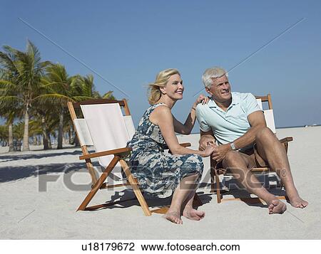Stock Image - Senior couple on sunloungers on tropical beach. Fotosearch