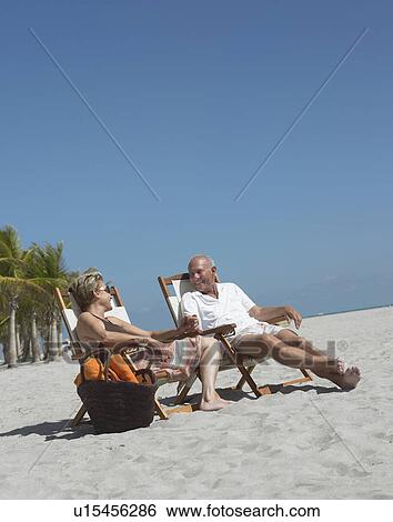 Stock Photograph - Senior couple on sunloungers on tropical beach. Fotosearch