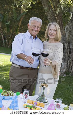 Stock Photo - Senior couple raising toast while birthday party in garden. Fotosearch