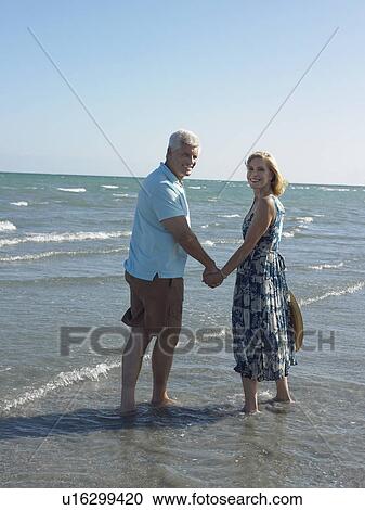 Stock Image - Senior couple walking on tropical beach, back view. Fotosearch