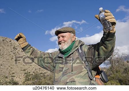 Stock Image - Senior male hiker raising arms and smiling. Fotosearch