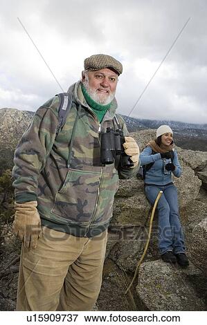 Stock Photo - Senior man holding binoculars in mountains. Fotosearch