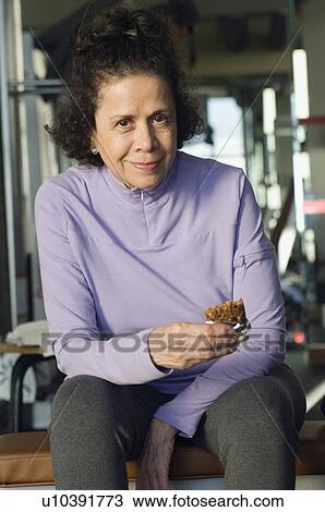 Stock Image - Senior Woman Eating Healthy Snack at Gym. Fotosearch