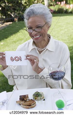 Stock Photo - Senior woman holding piece of paper with her age written on it, smiling. Fotosearch