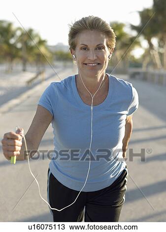 Stock Image - Senior woman jogging, holding mp3 player. Fotosearch