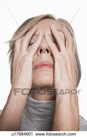 Stock Image - Senior woman with hands on face, close-up. Fotosearch