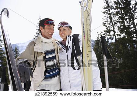 Skiing couple holding skis standing in mountains View Large Photo Image Stock Photo - Skiing couple holding skis standing in mountains. Fotosearch