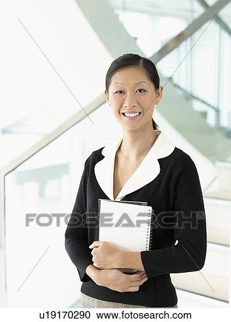 Smiling businesswoman standing, holding notebook View Large Photo Image Stock Image - Smiling businesswoman standing, holding notebook. Fotosearch