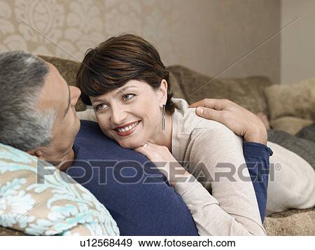 Stock Photo - Smiling couple relaxing on sofa in living room. Fotosearch