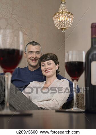 Smiling couple sitting at table in living room, wine glasses on foreground, (portrait) View Large Photo Image Stock Image - Smiling couple sitting at table in living room, wine glasses on foreground, (portrait). Fotosearch