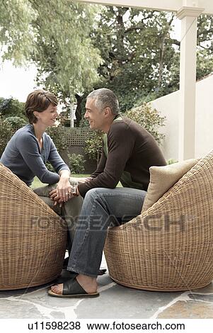 Smiling couple sitting on wicker chairs on patio View Large Photo Image Stock Photo - Smiling couple sitting on wicker chairs on patio. Fotosearch