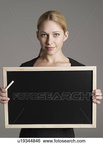 Stock Photograph - Smiling female teacher holding blackboard and chalk, portrait. Fotosearch