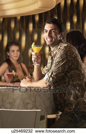 Smiling Man holding cocktail, standing at bar, side view View Large Photo Image Stock Image - Smiling Man holding cocktail, standing at bar, side view. Fotosearch