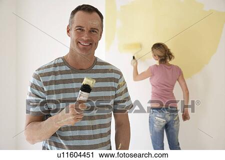 Smiling man holding paintbrush while woman paints wall with roller View Large Photo Image Stock Image - Smiling man holding paintbrush while woman paints wall with roller. Fotosearch