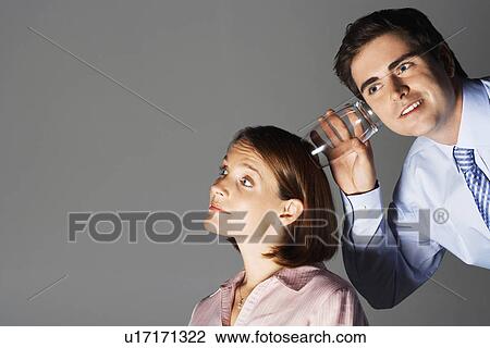 Stock Image - Smiling man listening through glass to smiling woman's head. Fotosearch