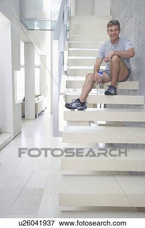 Smiling mid-adult man sitting on staircase, holding bottle of water View Large Photo Image Stock Photo - Smiling mid-adult man sitting on staircase, holding bottle of water. Fotosearch
