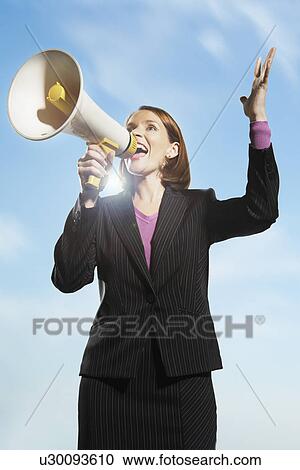 Stock Image - Smiling, Mid-adult woman shouting through megaphone outside. Fotosearch