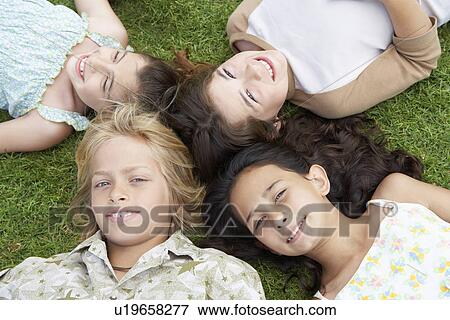 Stock Photo - Smiling Pre-teen Children Lying on backs in circle on Grass, overhead view. Fotosearch