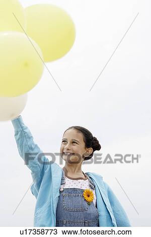 Stock Image - Smiling Pre-teen standing, arms raised, Holding Balloons. Fotosearch