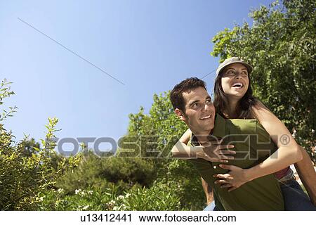 Stock Image - Smiling young couple, woman on man's back, portrait. Fotosearch