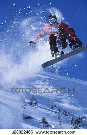 Stock Photograph - Snowboarder mid-air above ski Slope, snow powder trailing behind. Fotosearch