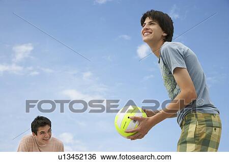 Stock Photograph - Teenage boys (16-17) playing beach volleyball, low angle view. Fotosearch