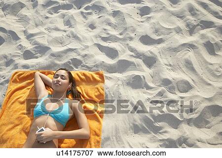 Stock Photo - Teenage girl (16-17) using mp3 player, lying on beach, view from above. Fotosearch