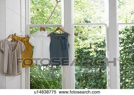 Stock Photography - Three blouses and skirt on hangers in domestic window. Fotosearch