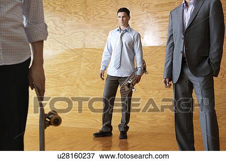 Three men standing, two holding skateboards, in front of interior wall View Large Photo Image Stock Photo - Three men standing, two holding skateboards, in front of interior wall. Fotosearch