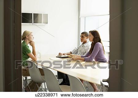 Stock Image - Three office workers sitting in conference room. Fotosearch
