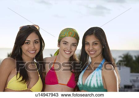Stock Image - Three teenage girls (16-17) wearing bikinis, portrait. Fotosearch