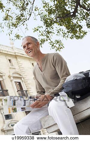 Tourist sitting in town square Reading Map, low angle view View Large Photo Image Stock Photo - Tourist sitting in town square Reading Map, low angle view. Fotosearch