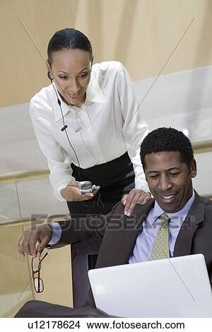 Two business people using laptop and mobile phone View Large Photo Image Picture - Two business people using laptop and mobile phone. Fotosearch