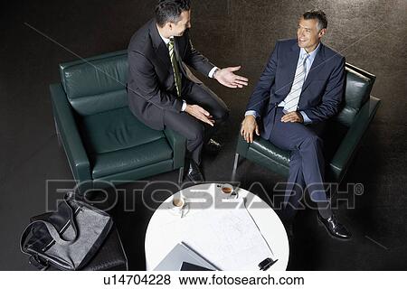 Stock Photo - Two businessmen sitting at table, talking, elevated view. Fotosearch