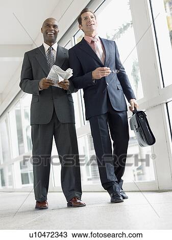 Stock Image - Two businessmen walking in hallway, (low angle view). Fotosearch