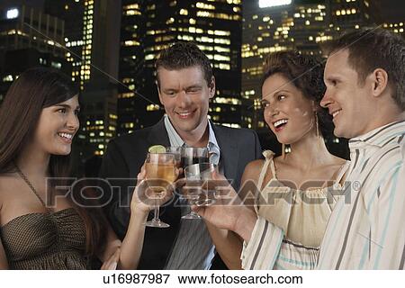 Stock Photo - Two elegant couples toasting against city night skyline. Fotosearch
