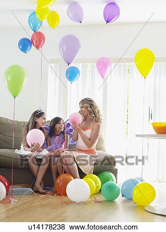 Two girls (7-9, 10-12) with mother sitting on sofa in room full of balloons View Large Photo Image Stock Photo - Two girls (7-9, 10-12) with mother sitting on sofa in room full of balloons. Fotosearch