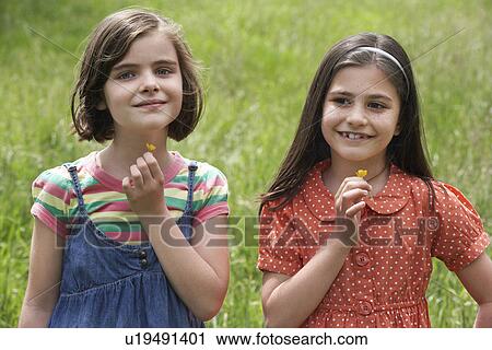 Two girls (7-9) holding flowers in field, portrait View Large Photo Image Stock Image - Two girls (7-9) holding flowers in field, portrait. Fotosearch