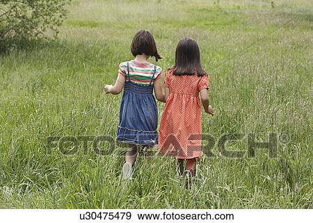 Stock Photo - Two girls (7-9) holding hands in field. Fotosearch