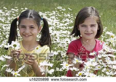 Stock Photo - Two girls(7-9) standing among flowers in meadow, portrait. Fotosearch