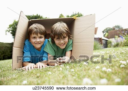 Stock Image - Two in backyard lying in cardboard box, portrait. Fotosearch