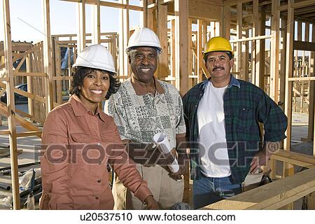 Stock Image - Two men and women with blueprints at construction site, portrait. Fotosearch