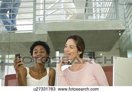Stock Image - Two mid-adult female office workers using mobile phone. Fotosearch