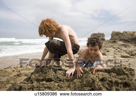 Two pre-teen boys playing in sand on beach View Large Photo Image Stock Photograph - Two pre-teen boys playing in sand on beach. Fotosearch