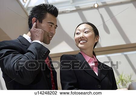 Stock Image - Two smiling business people walking in the hallway, indoors. Fotosearch