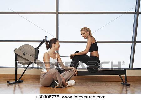 Two women talking at rowing machine in health club View Large Photo Image Stock Photography - Two women talking at rowing machine in health club. Fotosearch