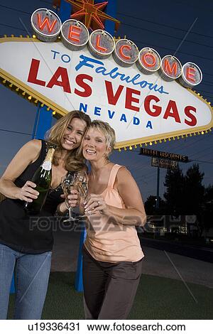 Stock Image - Two women toasting in front of Welcome to Las Vegas sign, portrait. Fotosearch