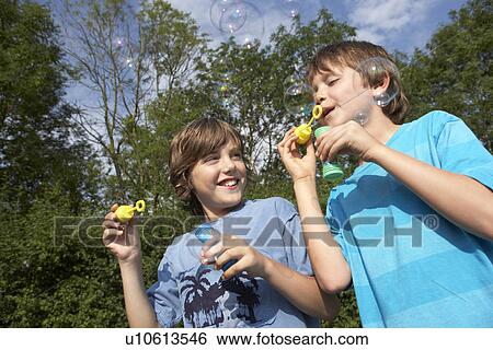 Two young boys blowing soap bubbles in park View Large Photo Image Stock Photograph - Two young boys blowing soap bubbles in park. Fotosearch