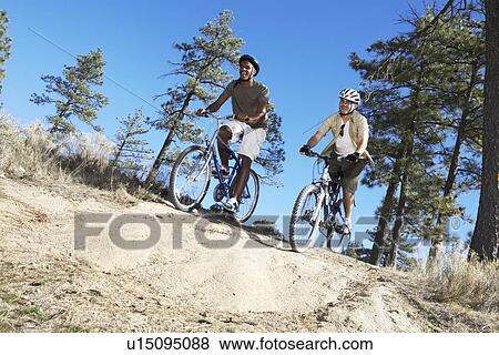 Two Young Men mountain biking on track through field, low angle view. View Large Photo Image Stock Photo - Two Young Men mountain biking on track through field, low angle view.. Fotosearch
