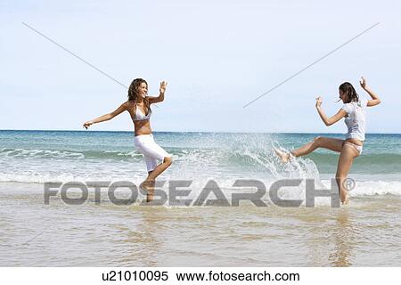 Stock Photography - Two Young Women Splashing Each Other on Beach. Fotosearch